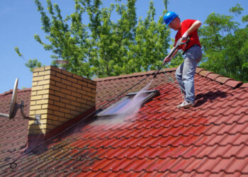 House roof cleaning with pressure tool. Worker on top of building washing tile with professional equipment. Moss removing with water.